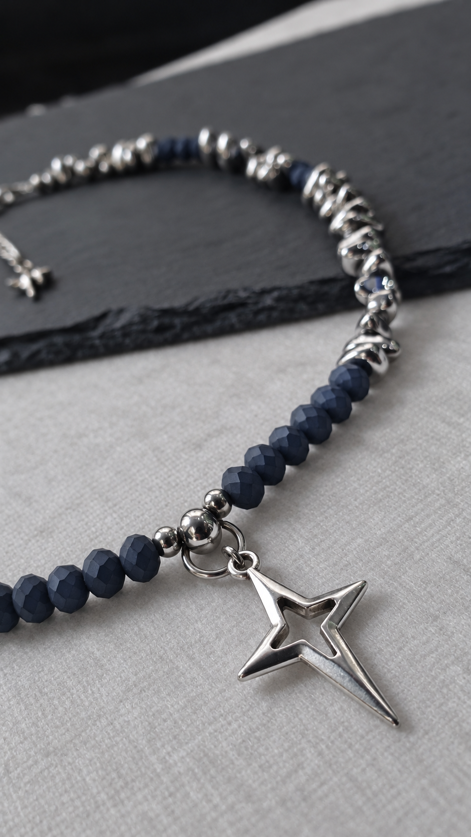 Angled close-up of NIGHTMARK's silver-plated North Star pendant with midnight blue crystal beads and silver hematite accents.