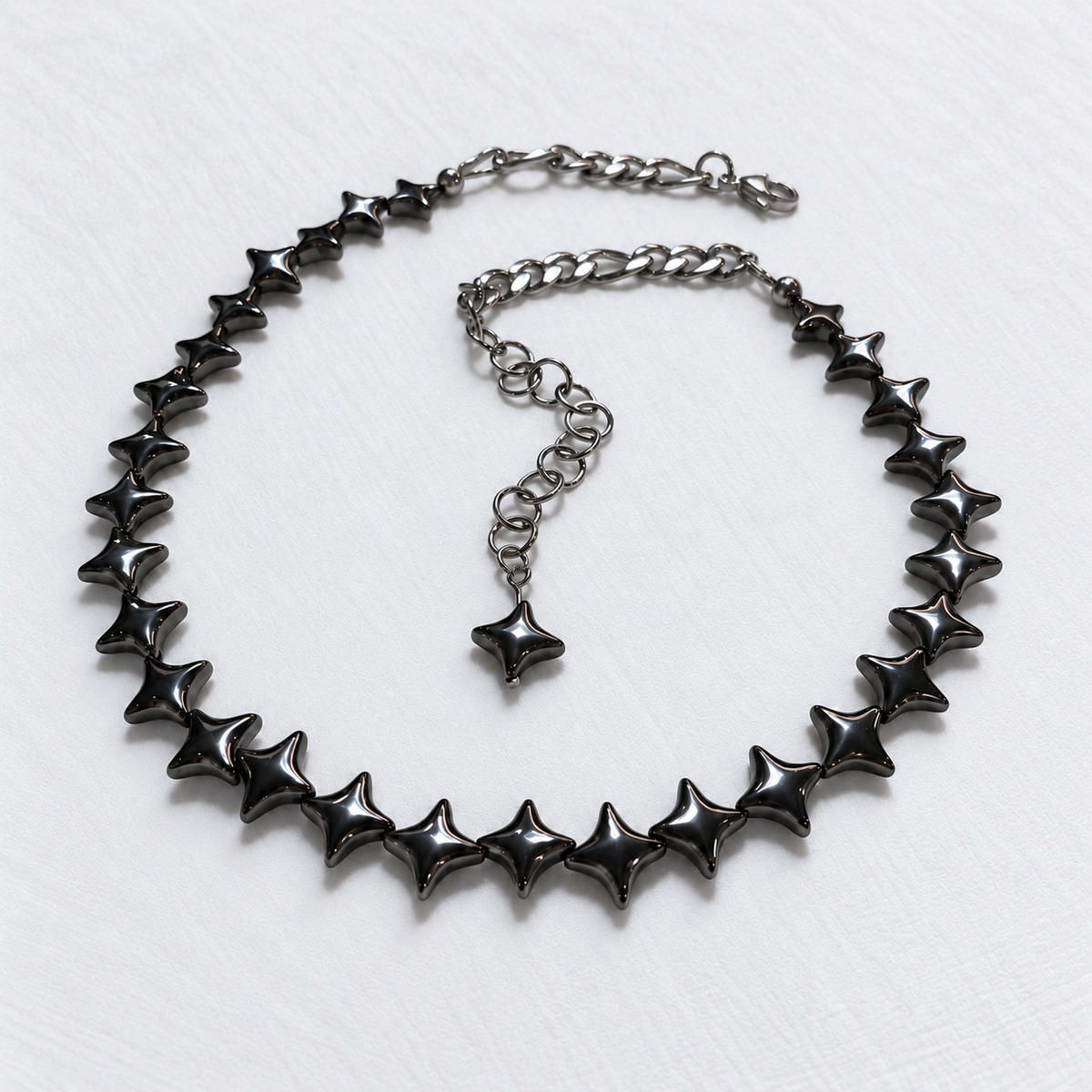 NORTHLINE Gunmetal North Star hematite choker with stainless steel rear chains and matching star-tipped extension on white fabric.