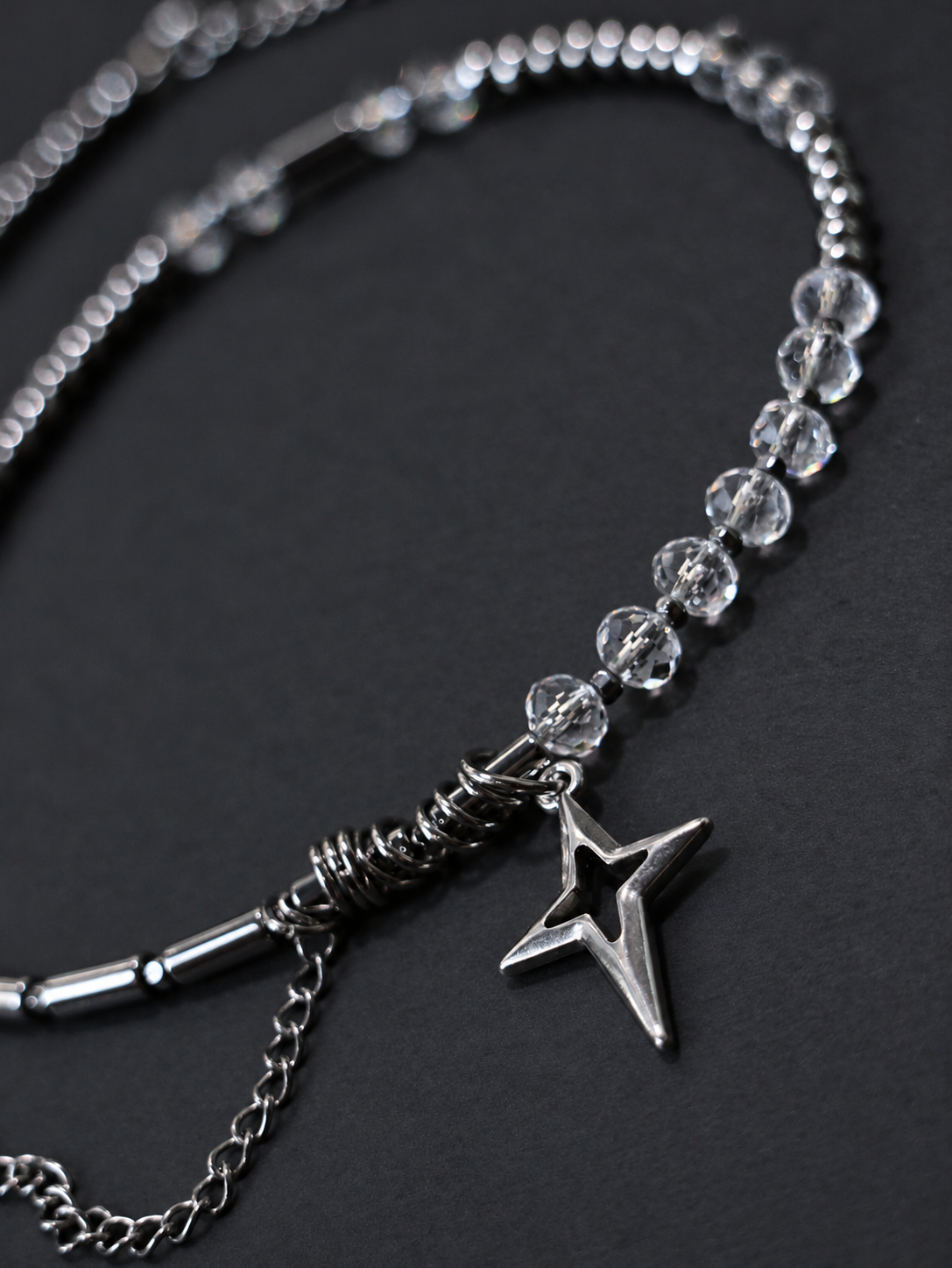 Close-up of SPECTRAL ARC's silver-plated North Star pendant, stainless steel ring detail and transparent faceted crystal beads.